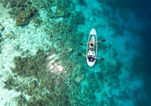 Aerial view of clear canoe gliding over vibrant coral reefs in the Maldives' turquoise waters.