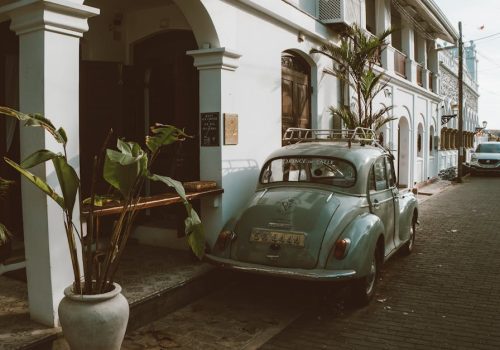 Vintage car parked on a charming street with colonial architecture and lush greenery.